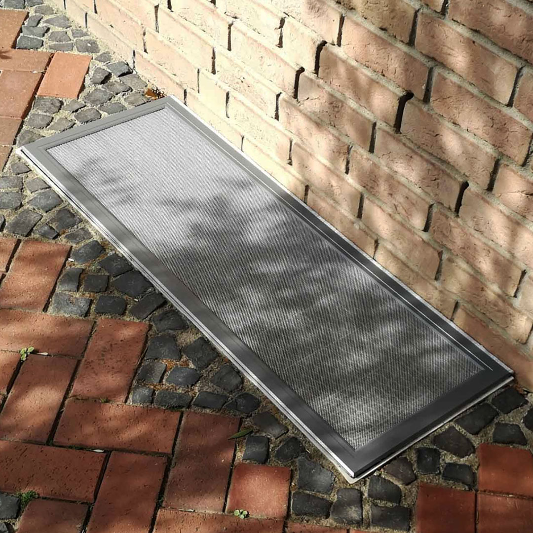 Lichtschachtschutz liegt auf neben roten Pflastersteinen