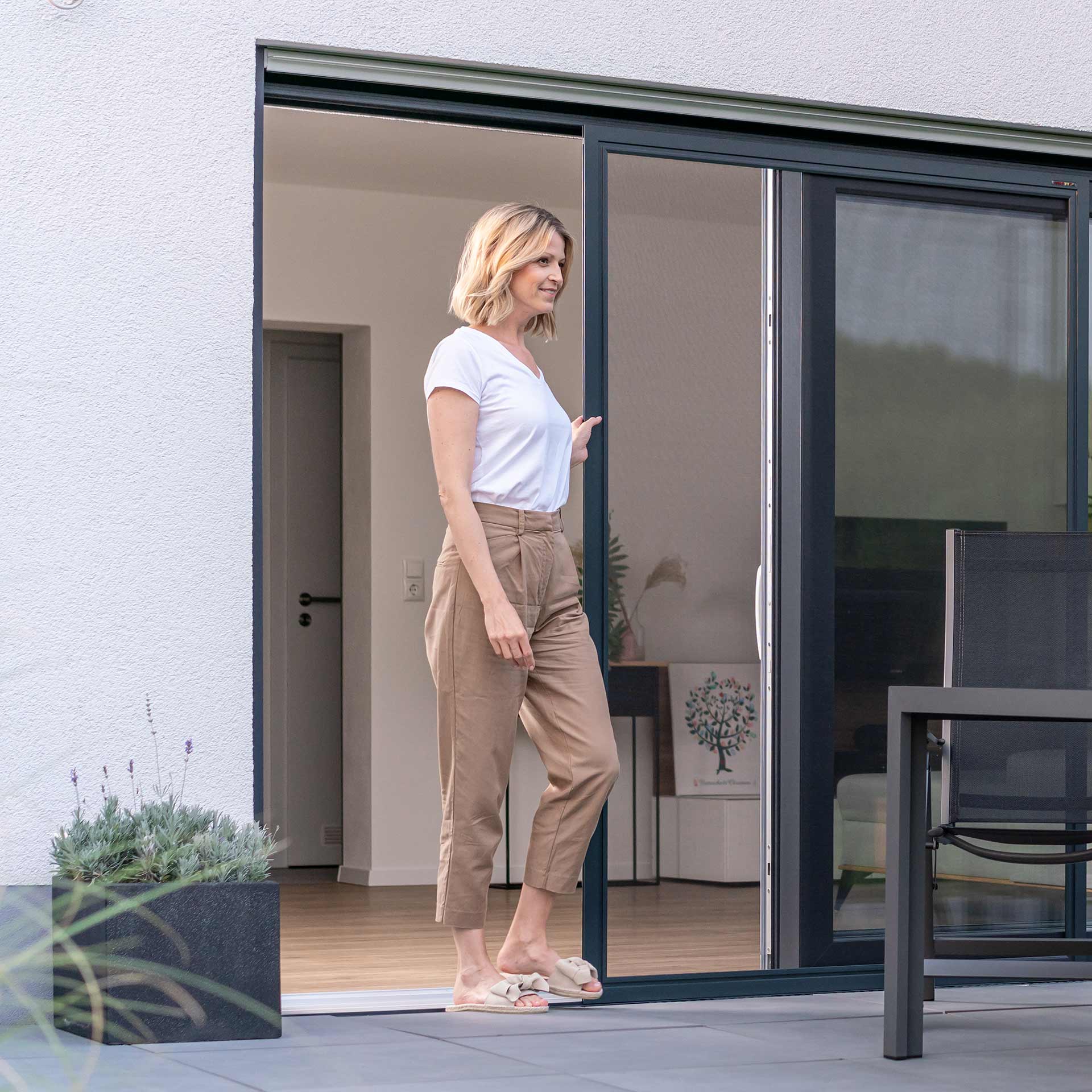 Frau geht durch Fliegengitterschiebetür auf Terrasse