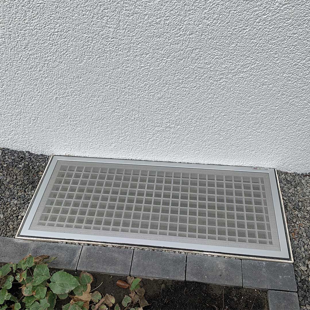 Lichtschachtabdeckung, installiert, zwischen Kiesweg und Gebäudewand