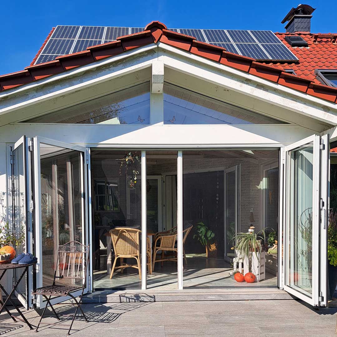 Wintergarten mit geöffneter Insektenschutzrollotür und Korbmöbeln