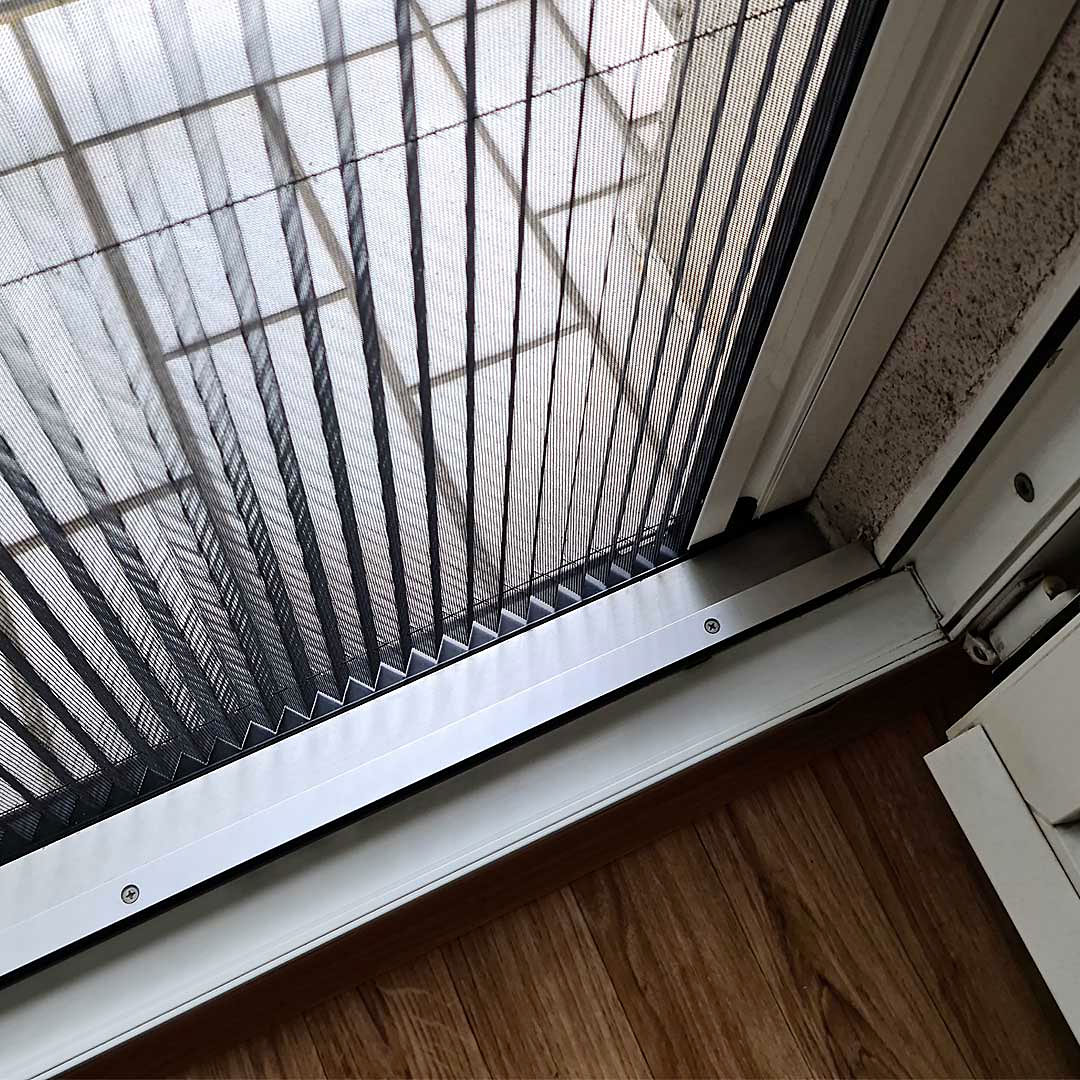 Geschlossenes Insektenschutzplissee vor einer Terrassentür auf Holzboden.
