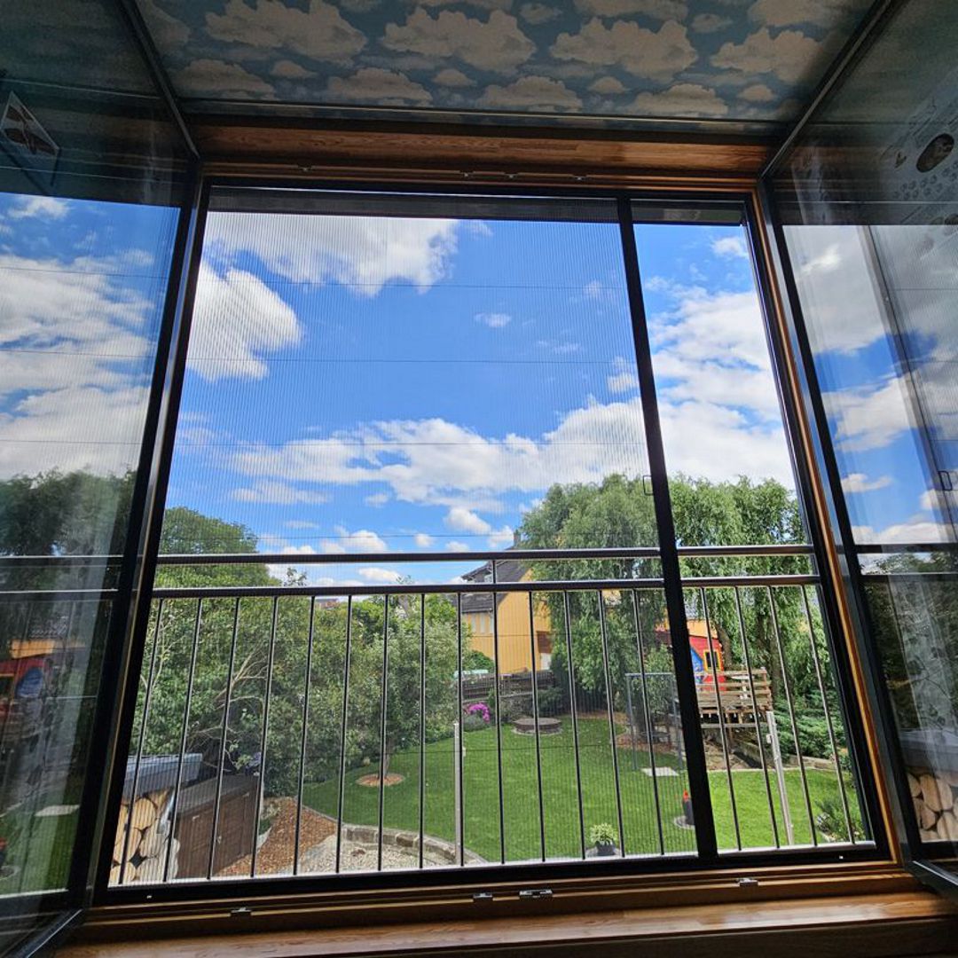 Fliegengitter schützt Fenster mit Blick in grünen Garten.