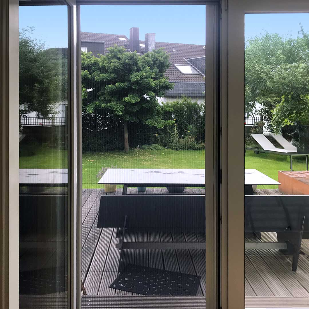 Terrassentür mit Fliegengitter mit Blick zum grünen Garten.