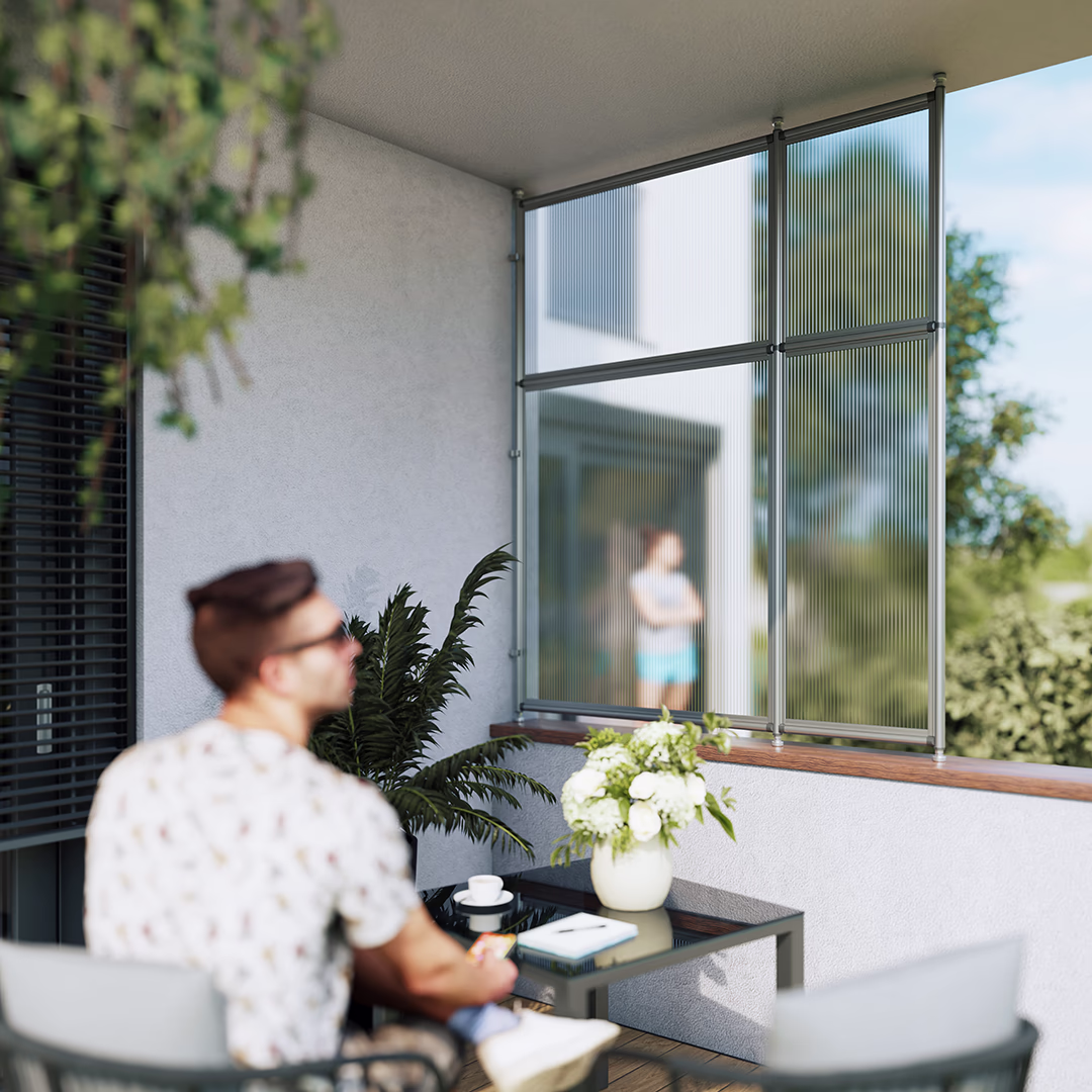 Pryvacy Wind- und Wetterschutz Grund-und Anbaumodule auf einer Brüstung montiert. In Vordergrund sitzt ein Mann entspannt im Freien. Durch die Hohlkammerplatten des Systems kann man verschwommen eine Person im Hintergrund erkennen.