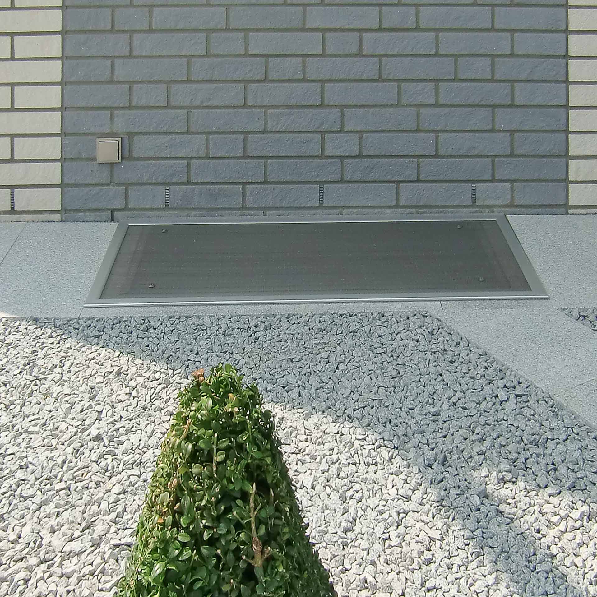 Lichtschatzschutz vor grauer Ziegelwand und Kies