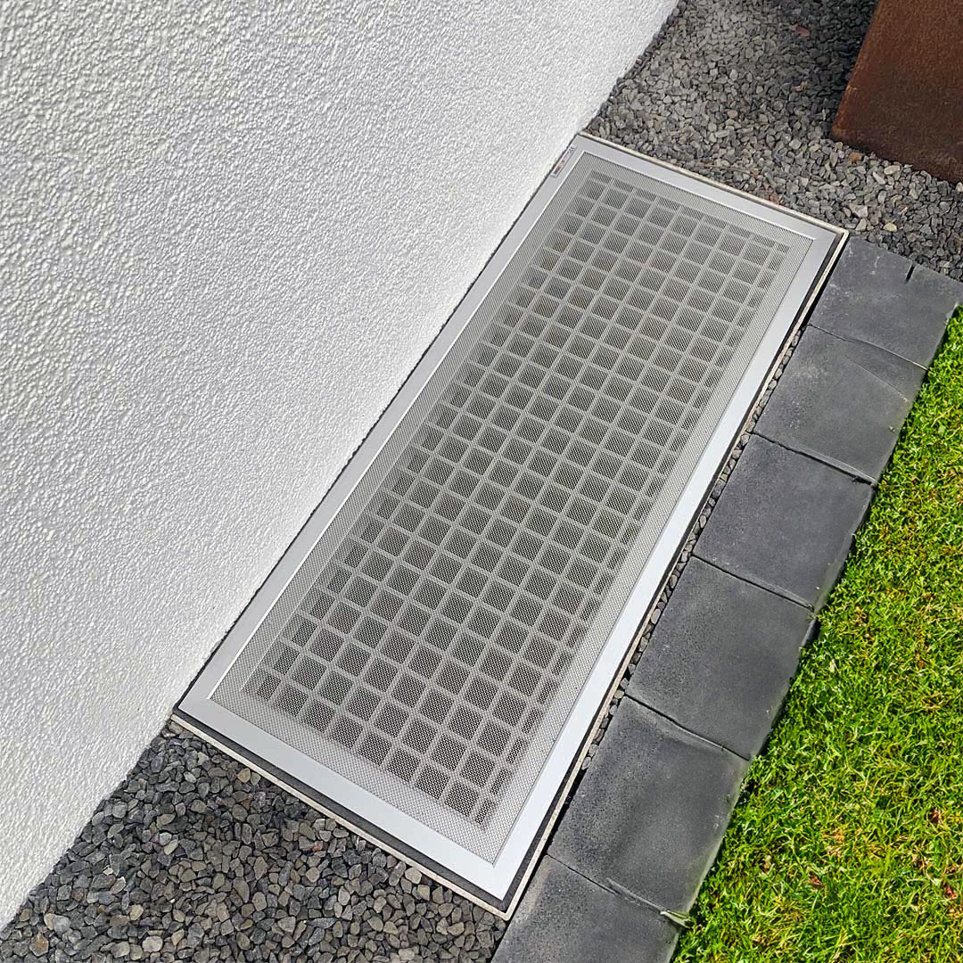 Lichtschachtabdeckung angrenzend an Wand und Rasen