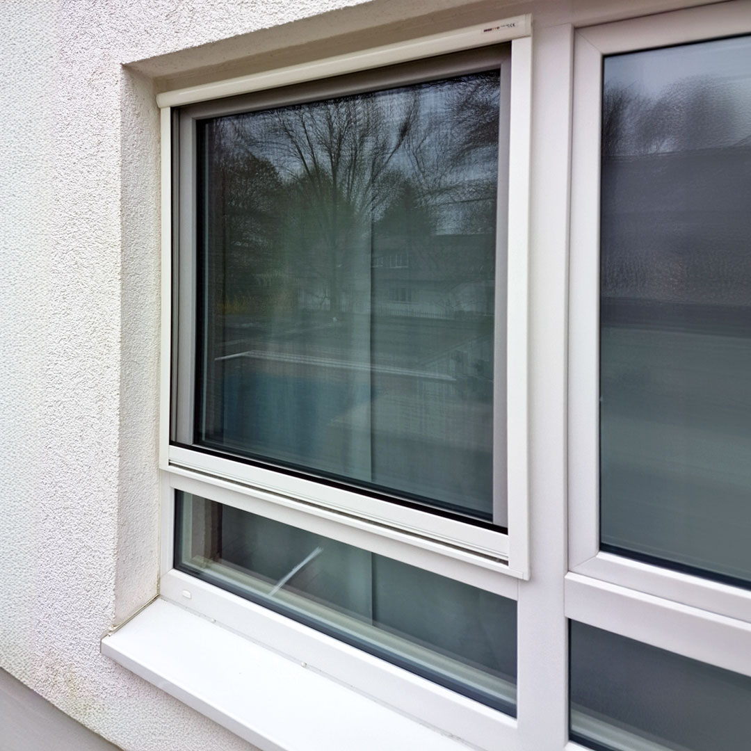 Fliegengitter vor geschlossenem Fenster am Gebäude.