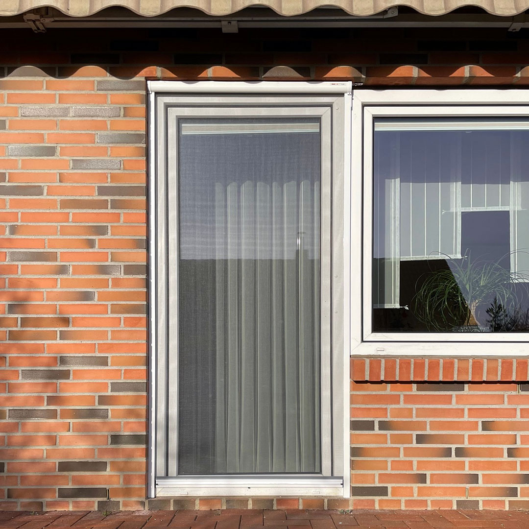 Fenstertür mit Fliegengitter, vor einer Ziegelwand montiert.