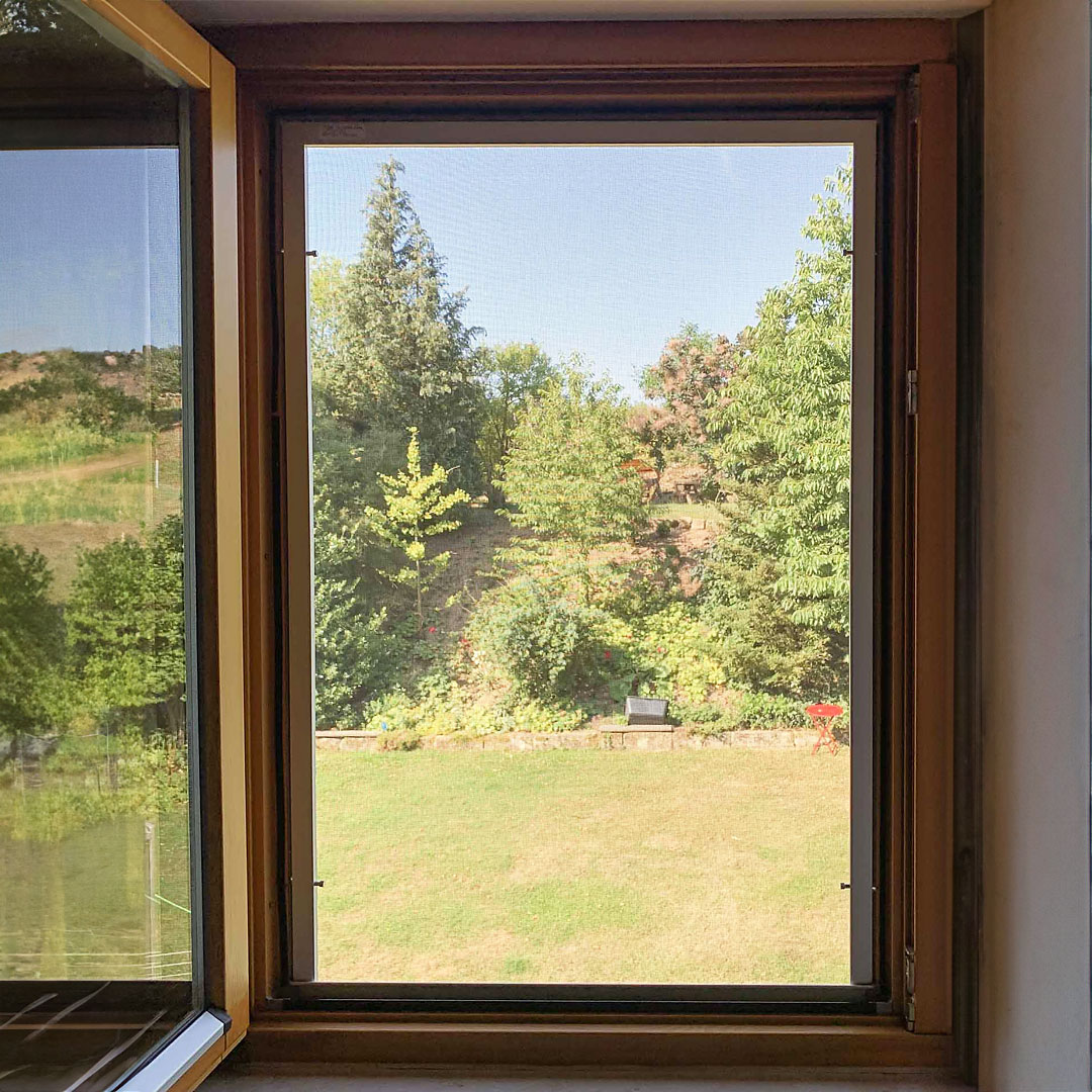 Fliegengitter am geöffneten Fenster, Blick auf grünen Garten.