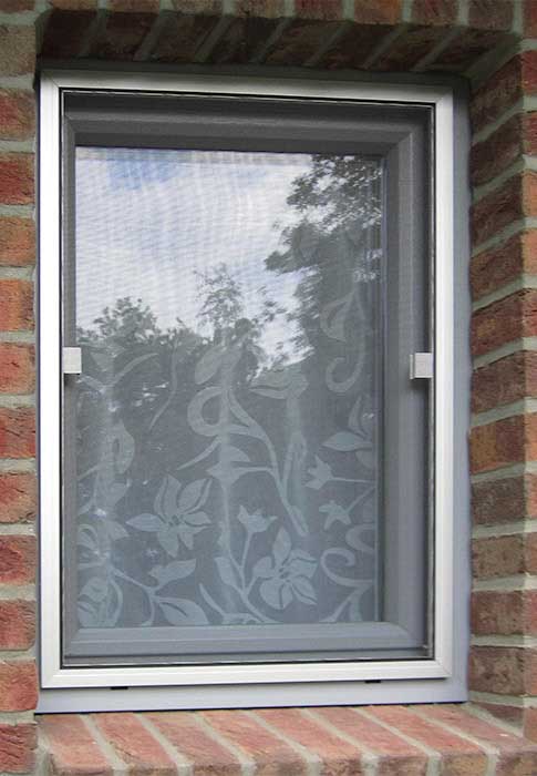 Fliegengitter schützt Fenster, eingebaut in Backsteinmauer.