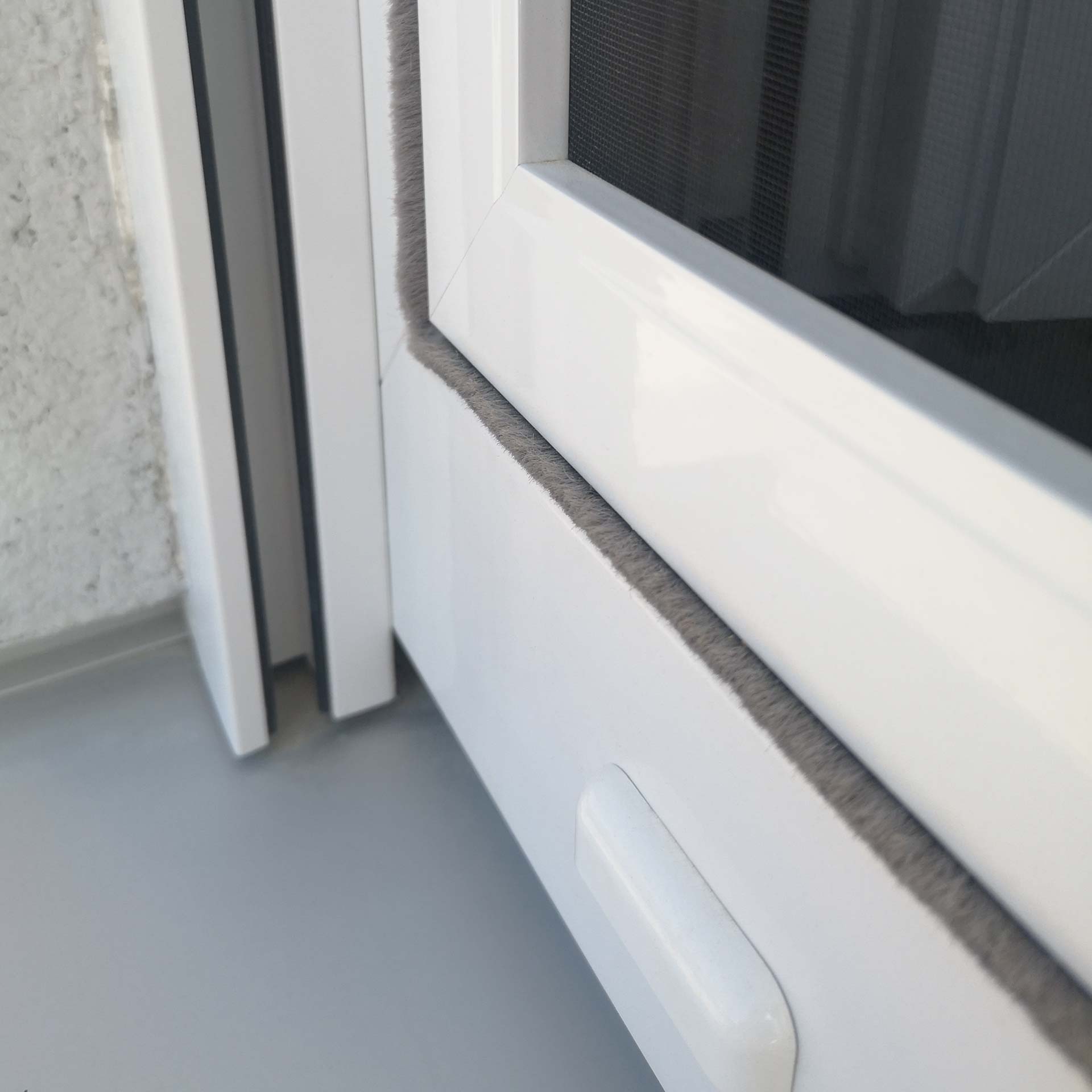 Fliegengitter befestigt an weißem Fensterrahmen.