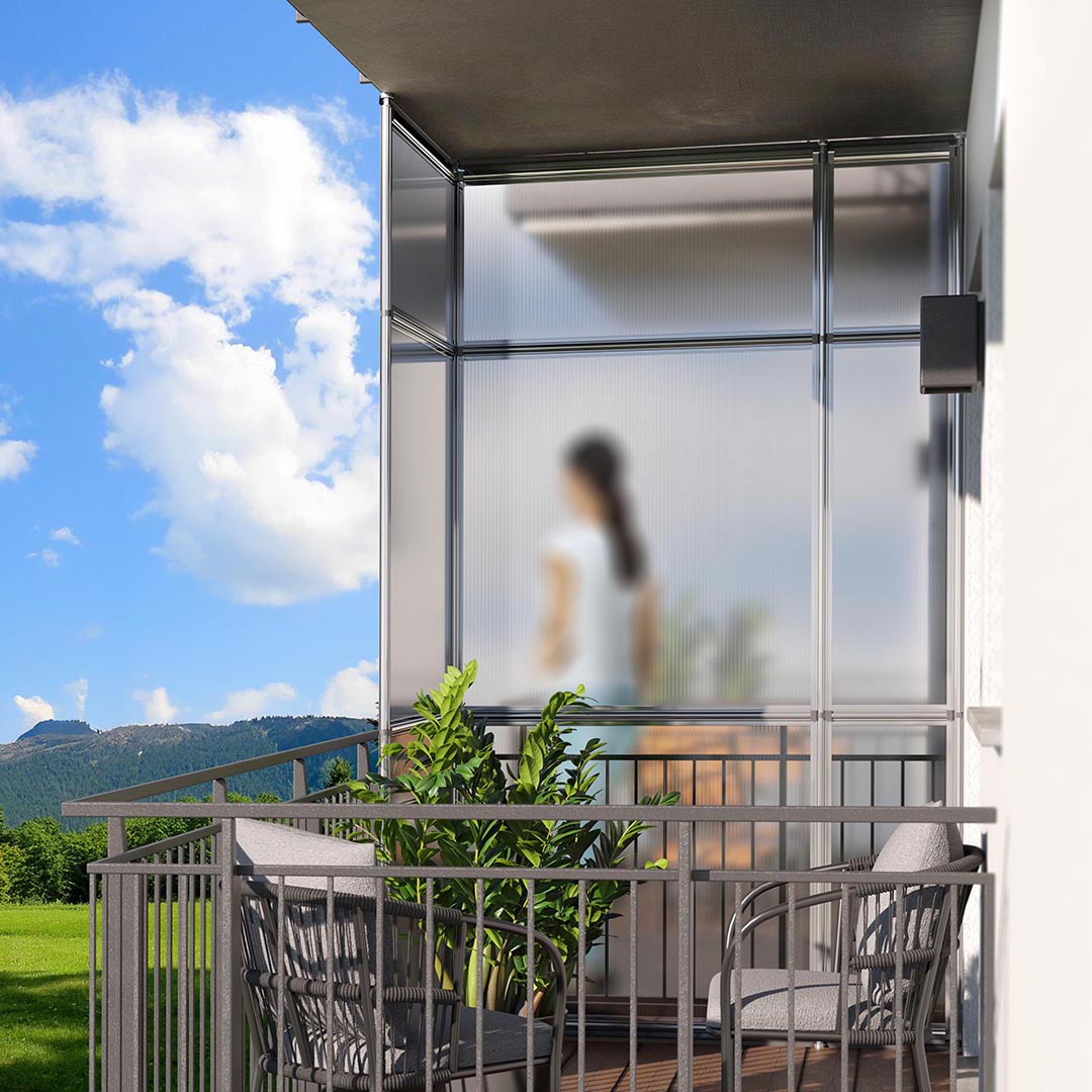 Frau steht auf möblierten Balkon vor Fensterfront.