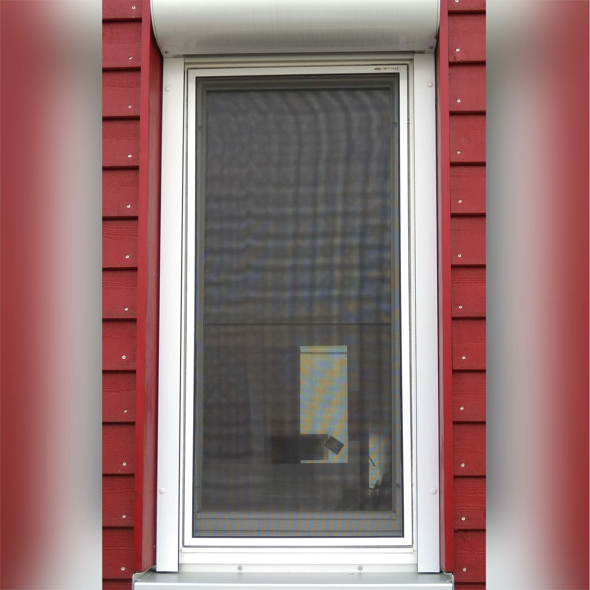 Fliegengitter an rotem Hausfenster mit weißem Rahmen.