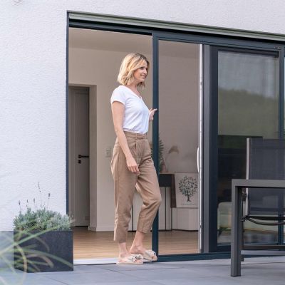 Frau geht durch Fliegengitterschiebetür auf Terrasse