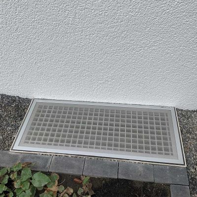 Lichtschachtabdeckung, installiert, zwischen Kiesweg und Gebäudewand