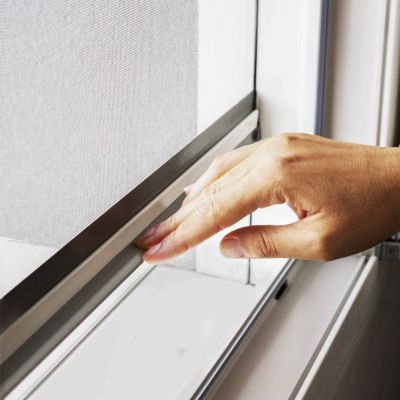 Hand schließt Fliegengitterrahmen an einem Fenster.