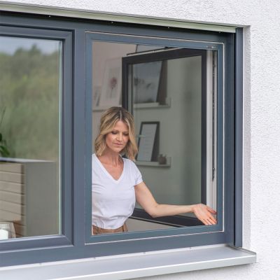 Frau befestigt Fliegengitter an offenem Fenster