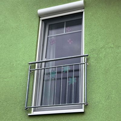 Fenster mit Fliegengitter in grüner Hauswand hinter Metallgeländer