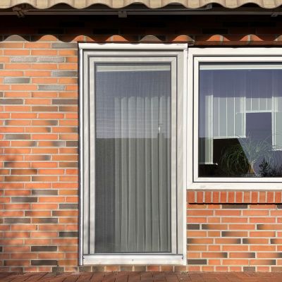 Fenstertür mit Fliegengitter, vor einer Ziegelwand montiert.