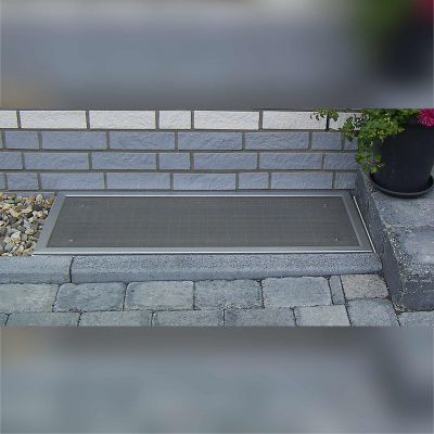 Lüftungsschachtabdeckung, vor gemauerter Hauswand auf Steinboden.