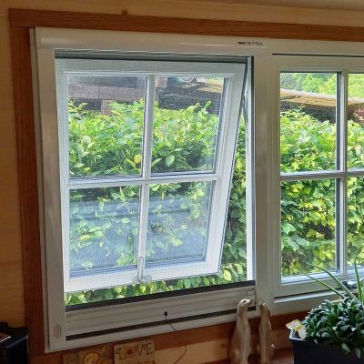Fensterflügel, offen, mit Fliegengitter, grüne Büsche draußen sichtbar.