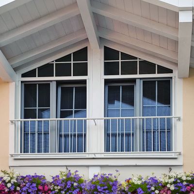 Fenster spiegelt Himmel, umrahmt von weißem Dach, Blumen unten.